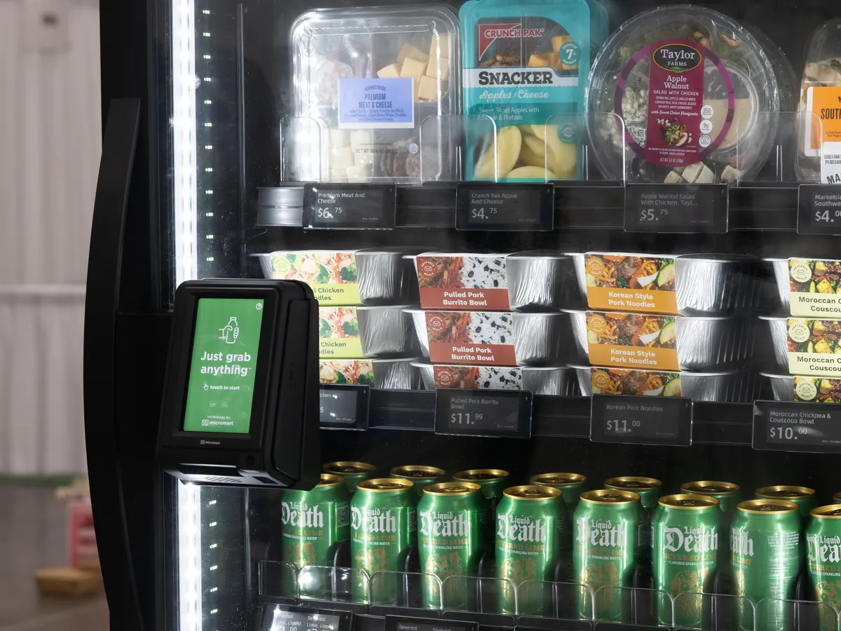 A smart cooler with a touchscreen on the door, shelves of snack packs, meal bowls, and canned drinks with digital price tags